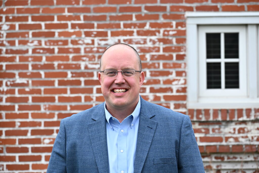 Rick Barley smiles in front of a brick building