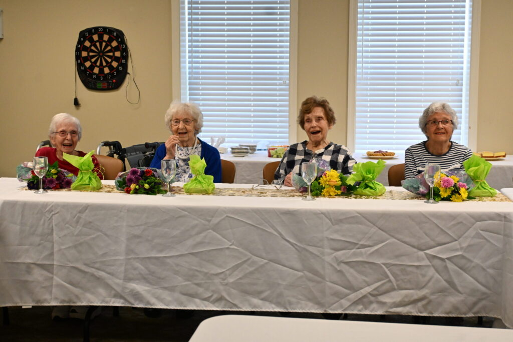 The four Centenarians being celebrated at Phoebe Richland smile and laugh at a table filled with gifts and food.