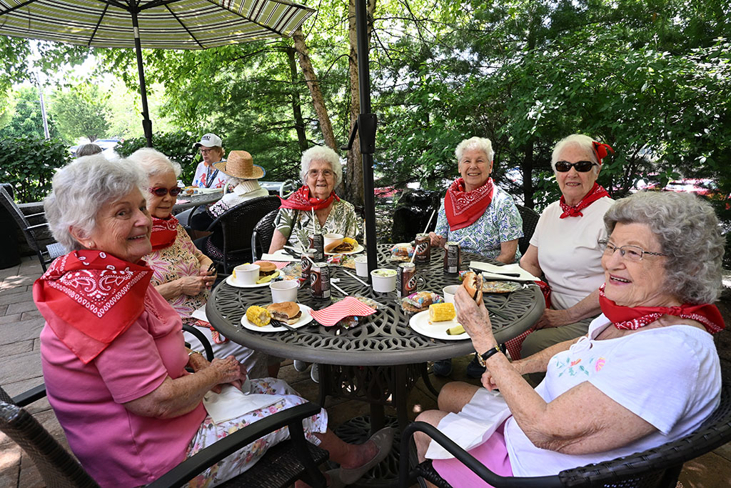 Residents smile around the table at the Terrace patio for the Cowboy Cookout. They adorn red bandanas and enjoy classic cookout food.