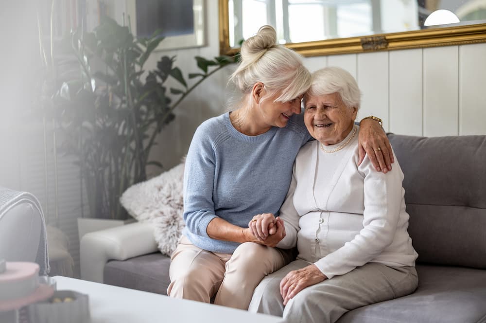 Two senior women smiling on a sofa, illustrating the community and senior living benefits.